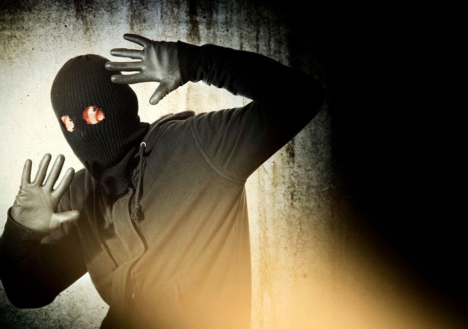 Catch the burglar concept, thief with balaclava caught in front of the grunge concrete wall.
