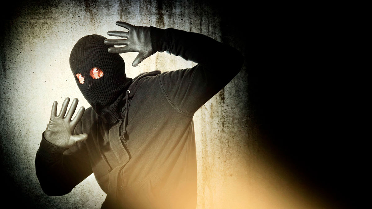 Catch the burglar concept, thief with balaclava caught in front of the grunge concrete wall.